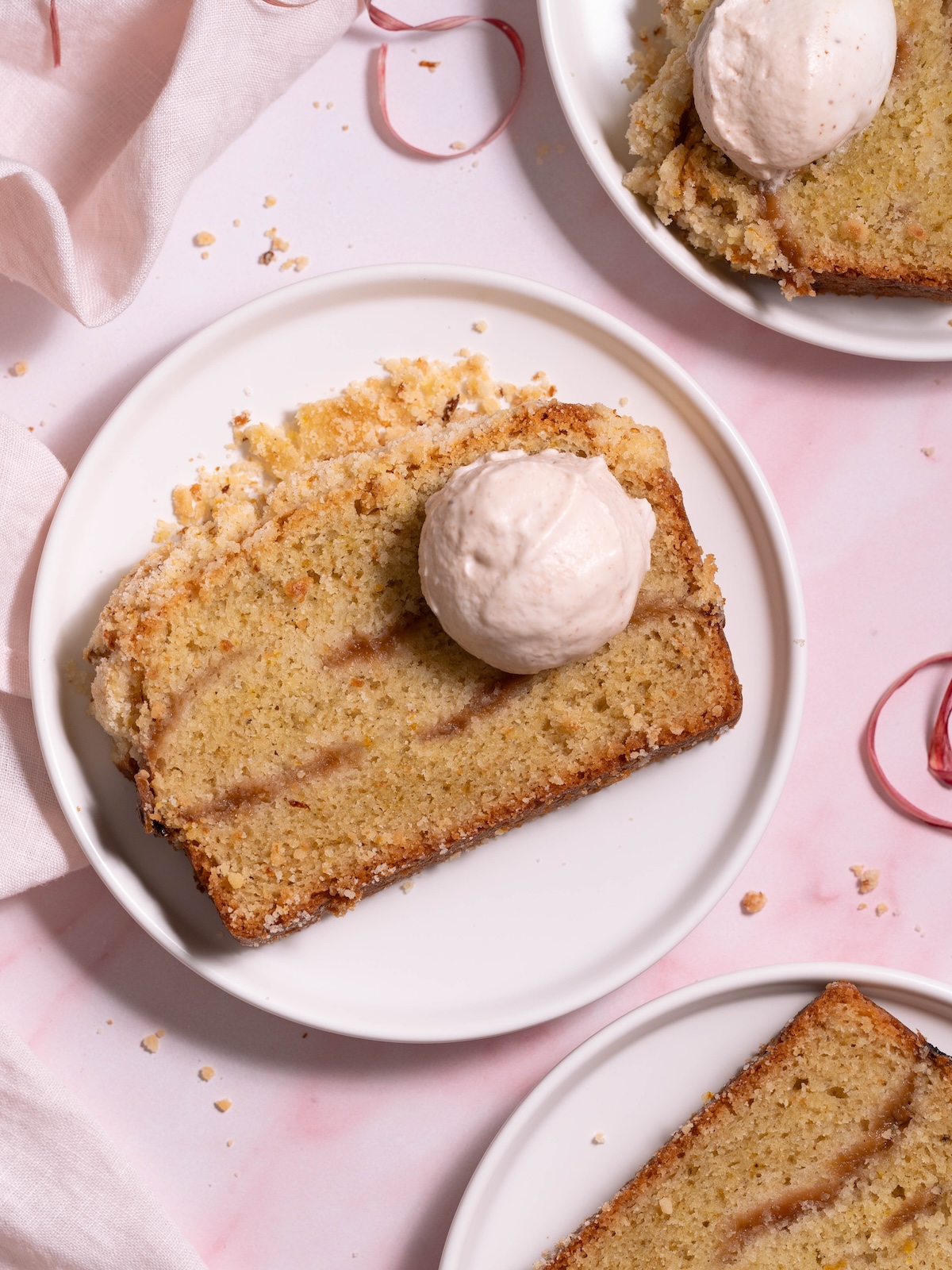 Slices of rhubarb crumble cake on white plates, served with dollops of magnolia whipped cream