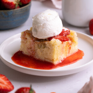 A slice of sourdough bread pudding topped with strawberries and whipped cream