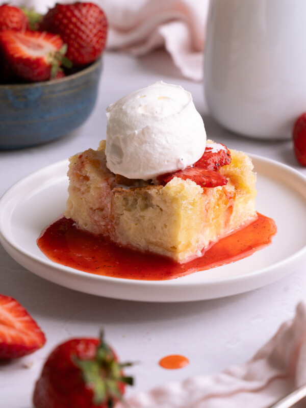 A slice of sourdough bread pudding topped with strawberries and whipped cream