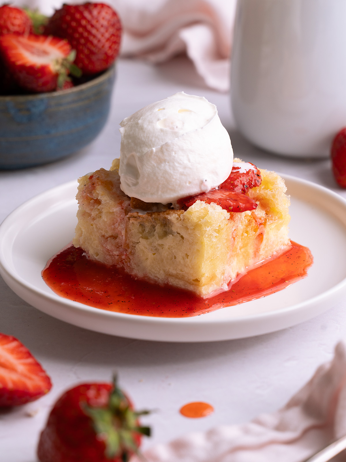 A slice of sourdough bread pudding topped with strawberries and whipped cream