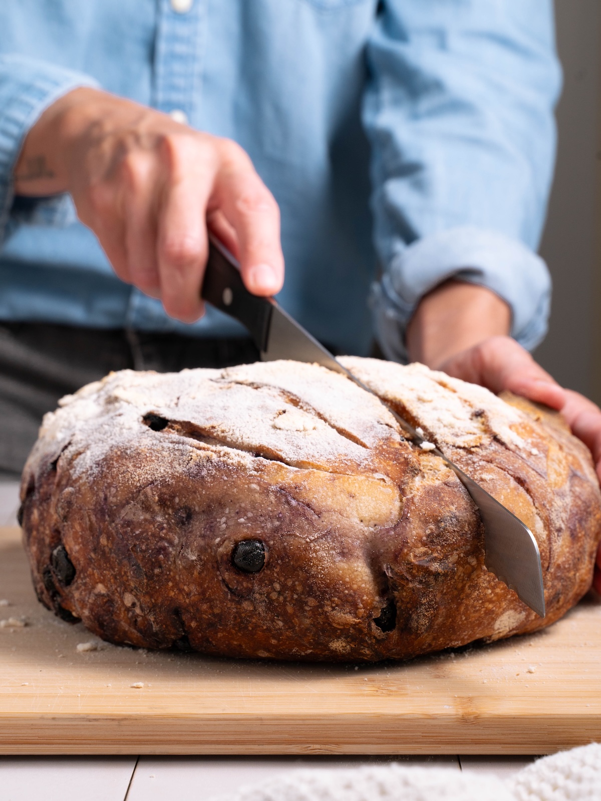 Slicing a homemade sourdough boule filled with dried blueberries