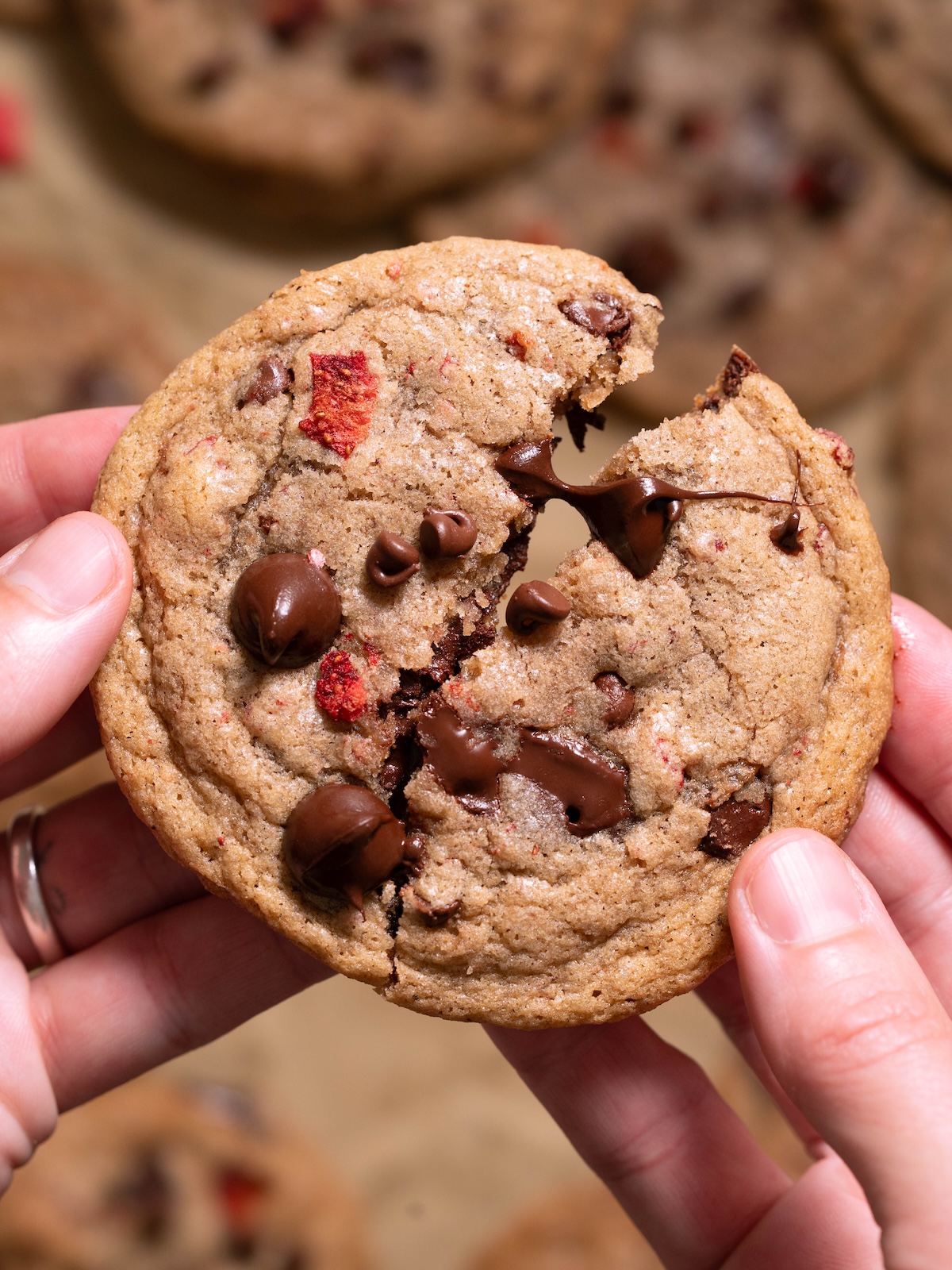 Hands breaking open a chocolate chip cookie filled with strawberries