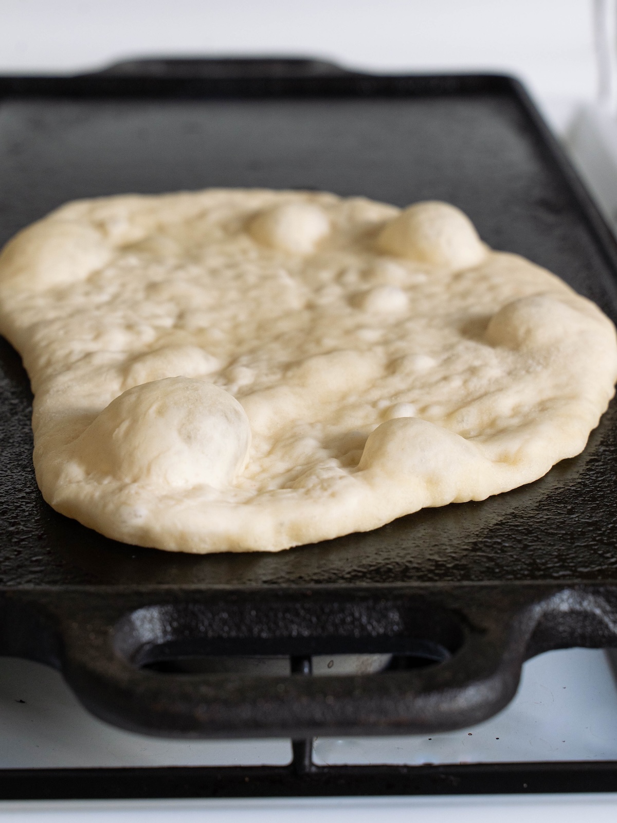 Bubbles forming on naan flatbread while cooking on a cast iron pan