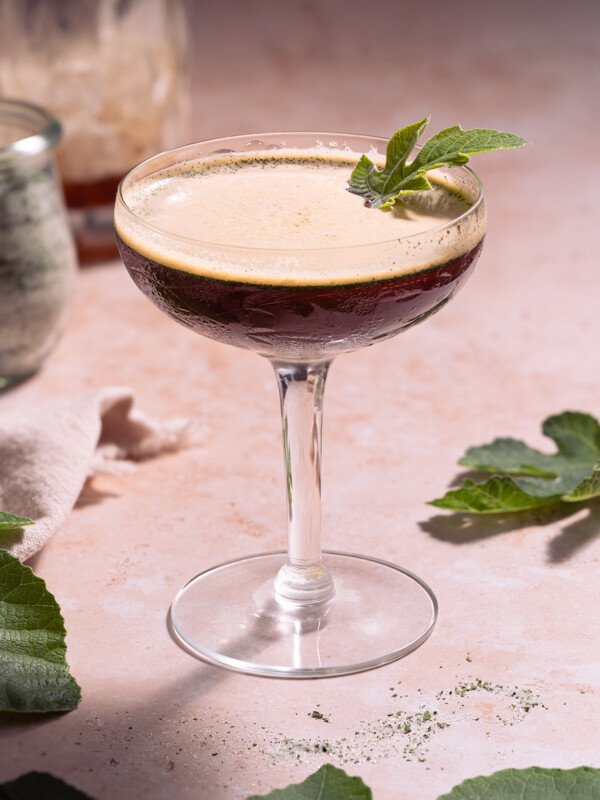 A fig leaf shakerato served in a coupe glass with a tiny fig leaf garnish