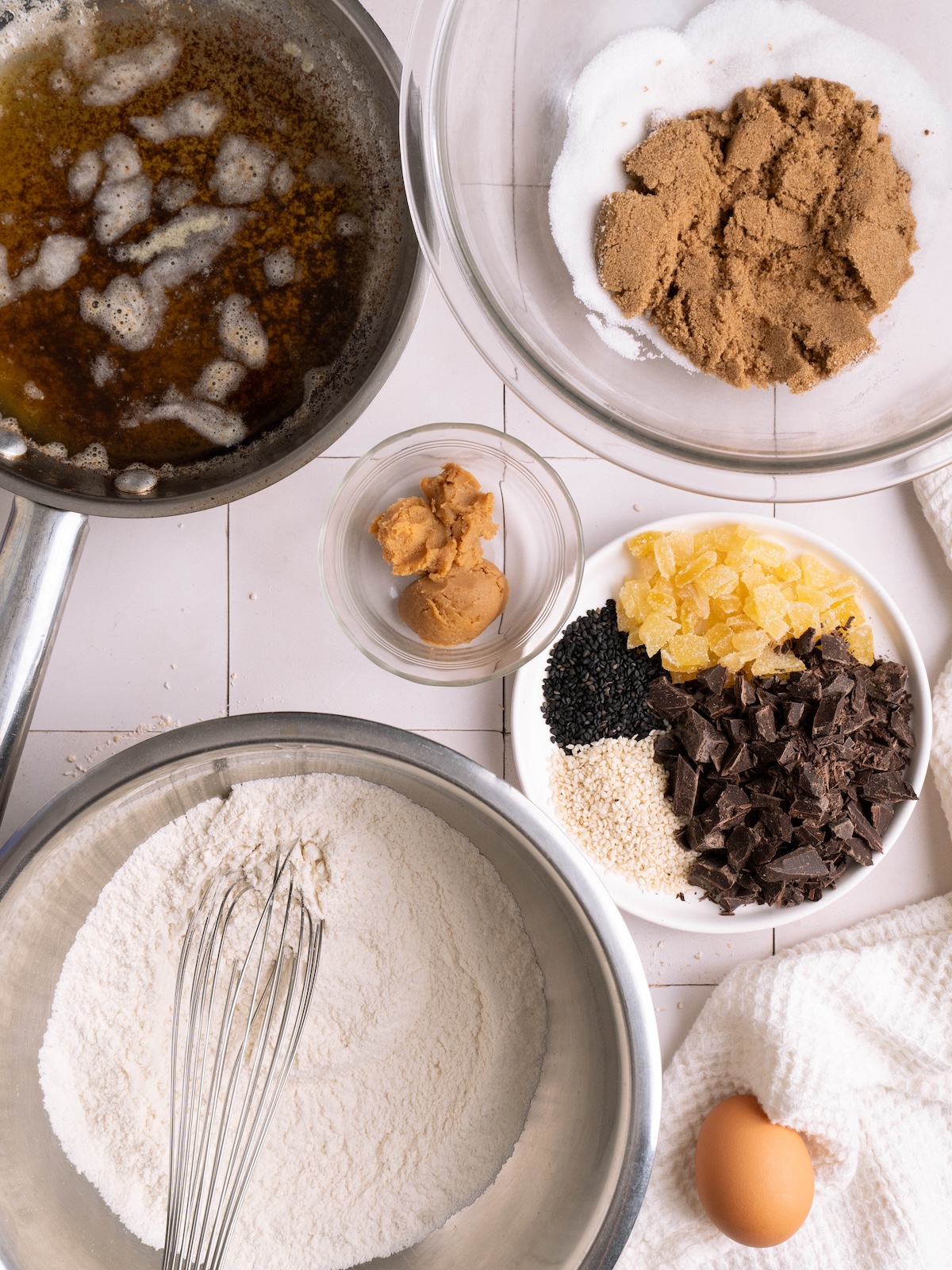 Bowls of ingredients for miso chocolate chip cookies, including candied ginger, sesame seeds, and brown butter