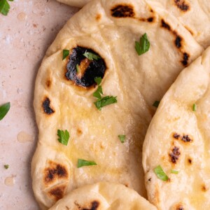 Pieces of homemade sourdough naan layered on top of each other, brushed with butter and herbs