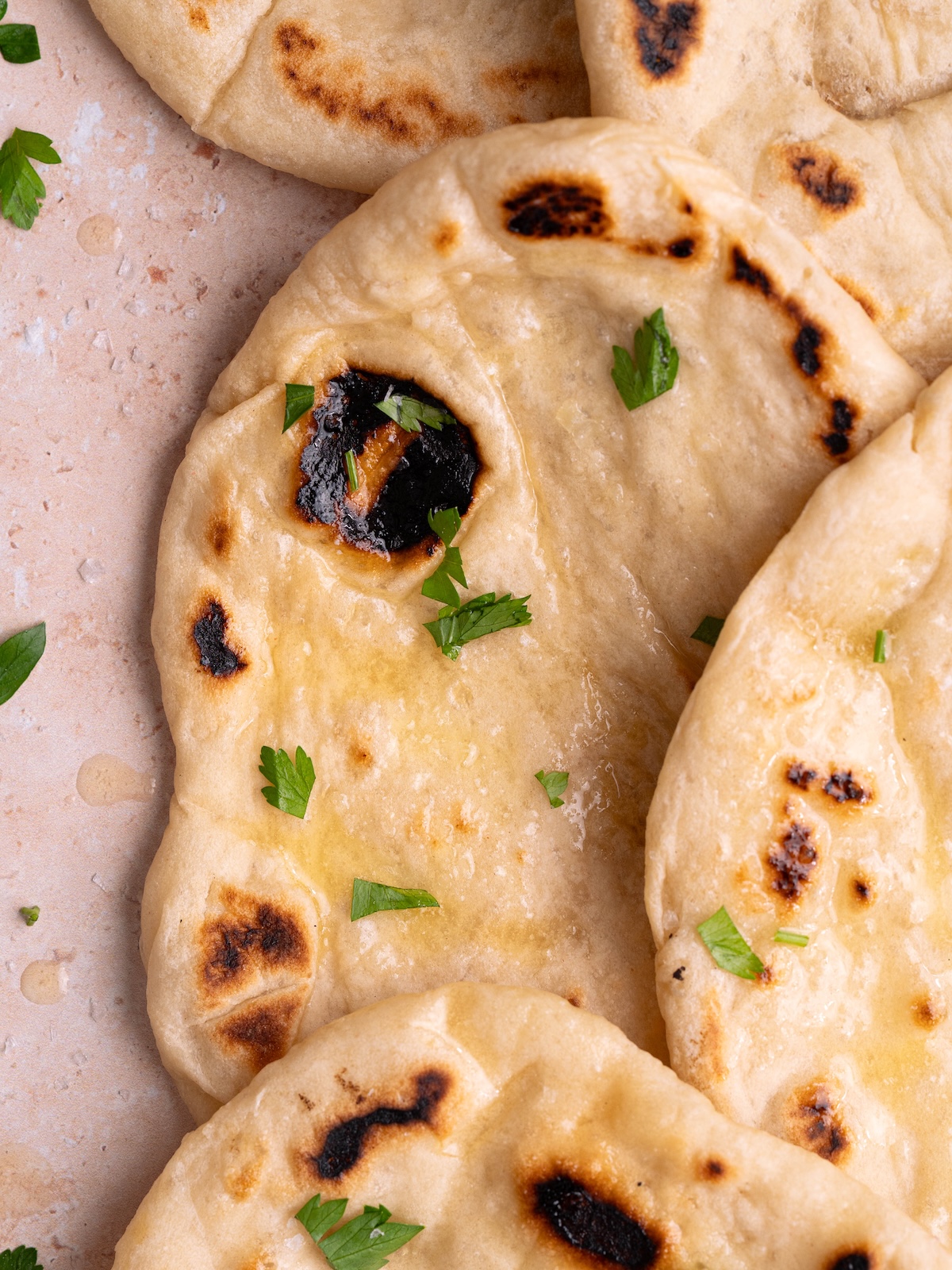Pieces of homemade sourdough naan layered on top of each other, brushed with butter and herbs