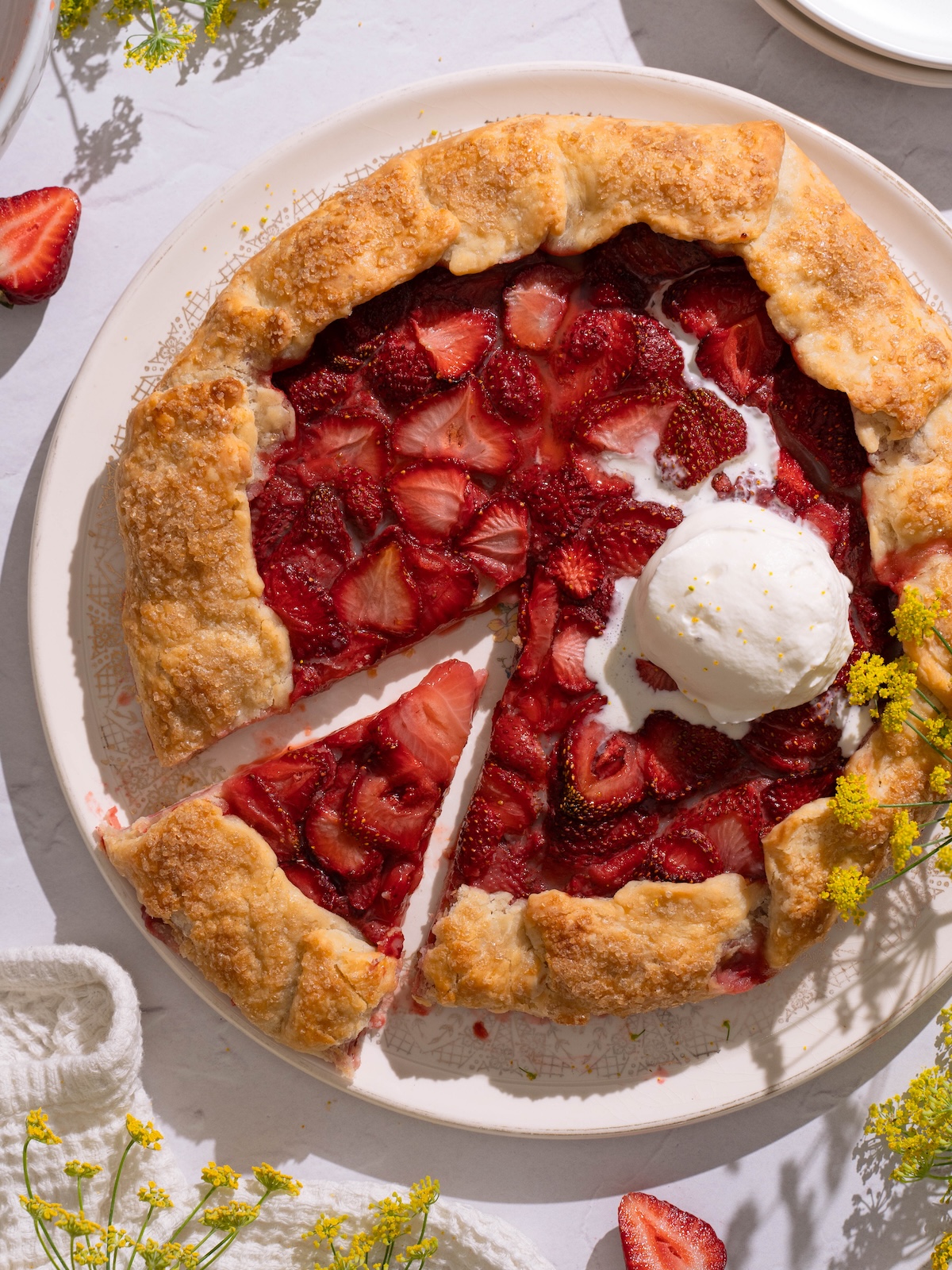 A strawberry fennel pollen galette on a serving plate, with fresh fennel flowers