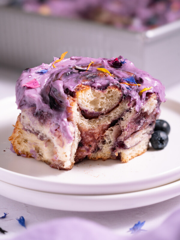A blueberry cinnamon roll on a plate with a bite taken out of it