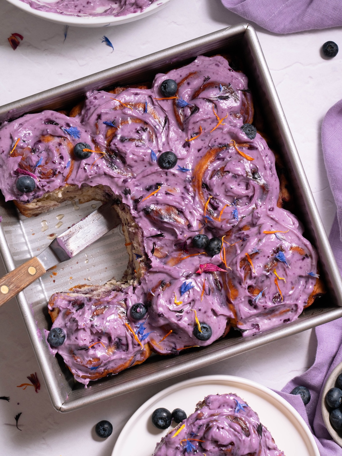 A pan of blueberry cinnamon rolls being served onto white plates