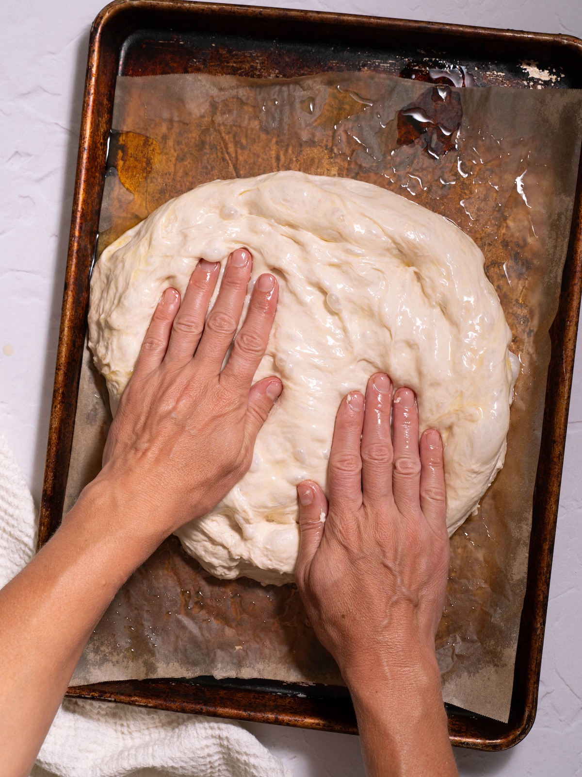Hands pressing focaccia into an oiled pan