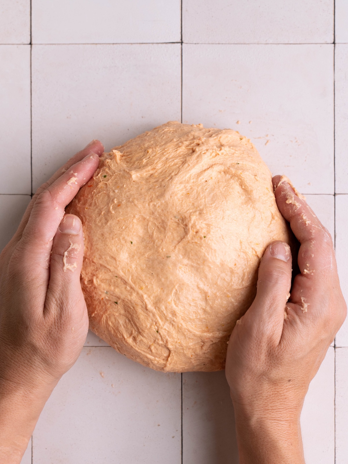 Hands shaping tomato sourdough into a rough ball
