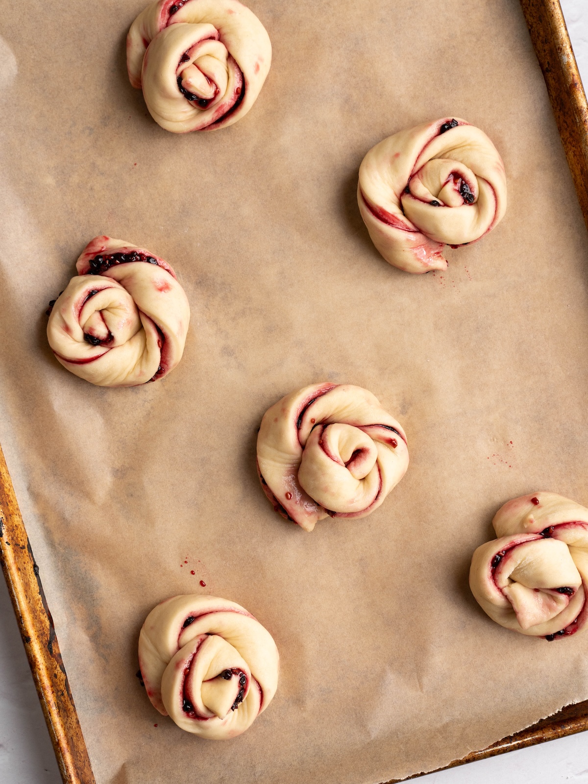 Twisted elderberry buns proofing on a baking sheet