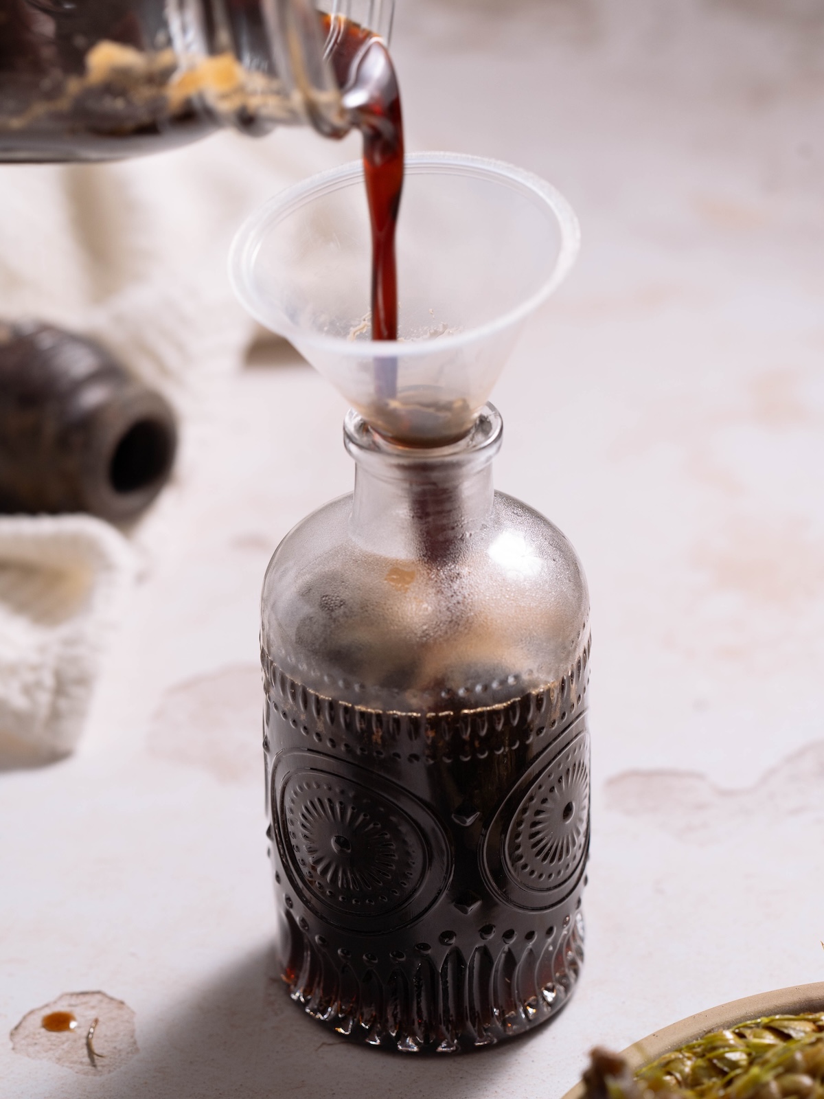 Pouring finished pine cone syrup into a decorative glass jar