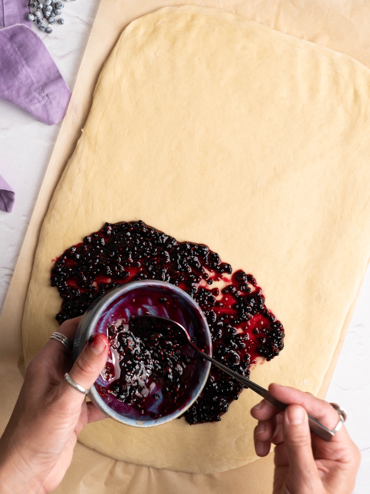 Spreading homemade elderberry jam onto sweet roll dough