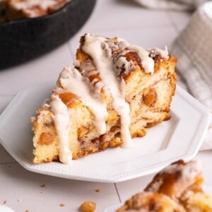 A slice of apple cinnamon roll on a plate with brown butter glaze dripping down the sides
