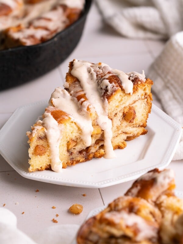 A slice of apple cinnamon roll on a plate with brown butter glaze dripping down the sides