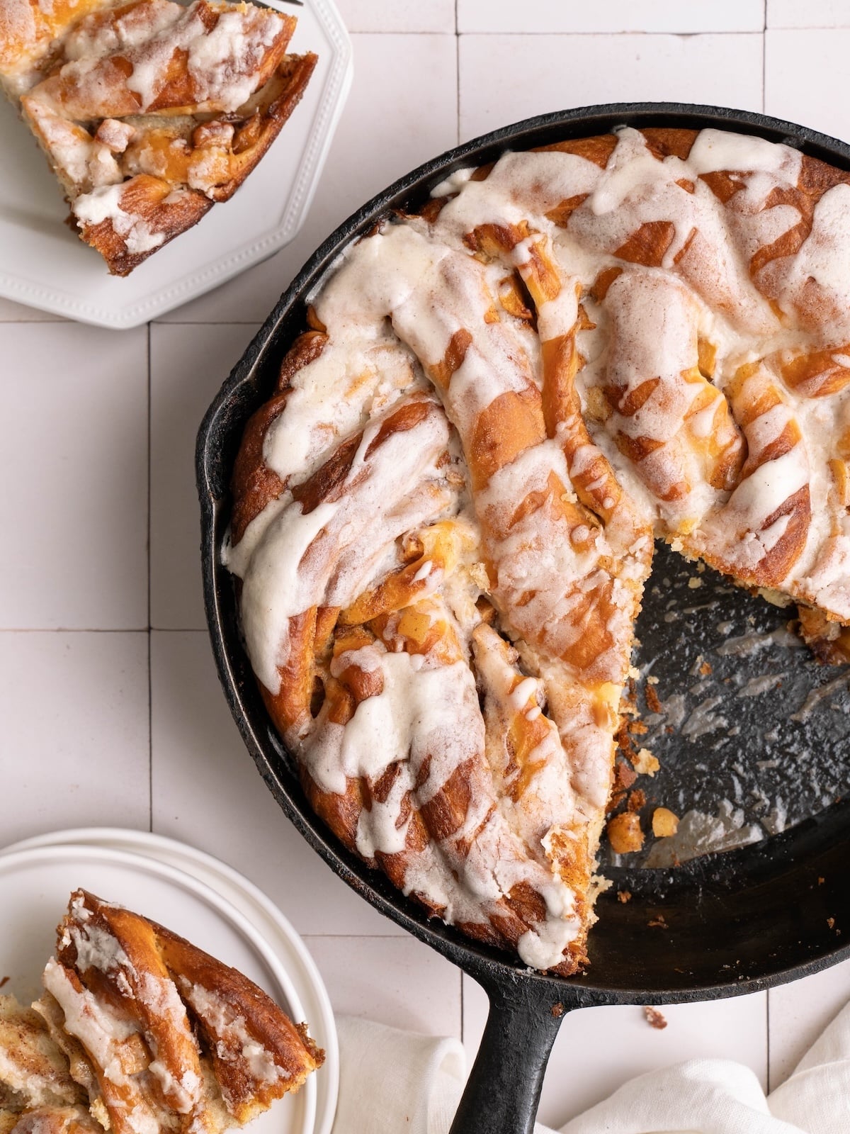 A big apple cinnamon roll in a cast iron pan, with slices served on the side